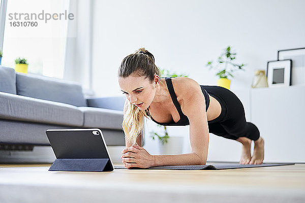 Frau  die zu Hause über ein digitales Tablet im Internet eine Plank-Übung lernt