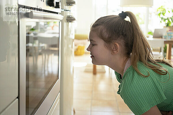 Lächelndes Mädchen  das den Ofen betrachtet  während es in der Küche steht