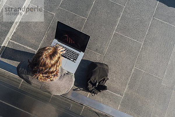 Junger männlicher Unternehmer  der einen Laptop benutzt  während er an einer Wand im Finanzbezirk an einem sonnigen Tag steht