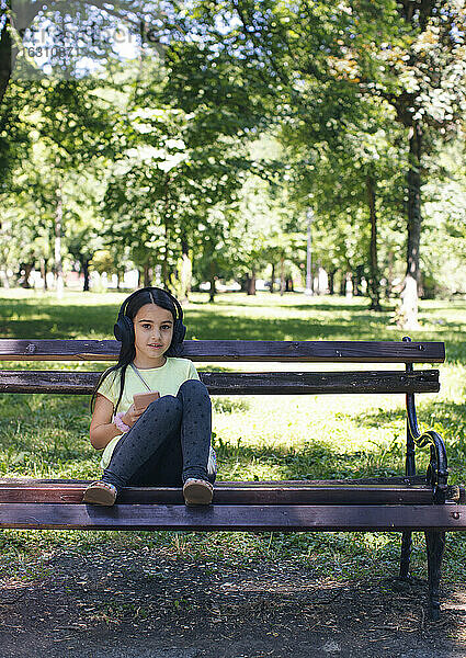 Nettes Mädchen mit Kopfhörer sitzt auf Bank im Park
