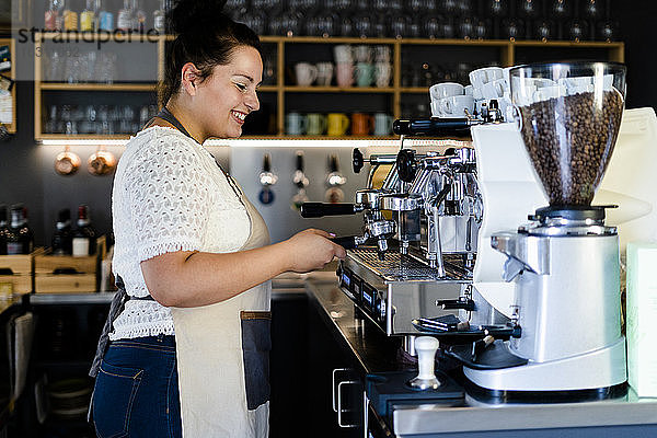 Lächelnde Barista-Frau  die Kaffee durch eine Maschine in einem Café zubereitet