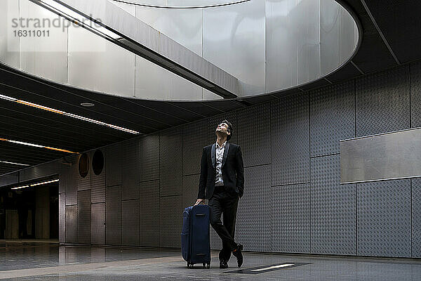 Nachdenklicher Geschäftsmann mit Koffer schaut durch ein Oberlicht  während er am Bahnhof steht