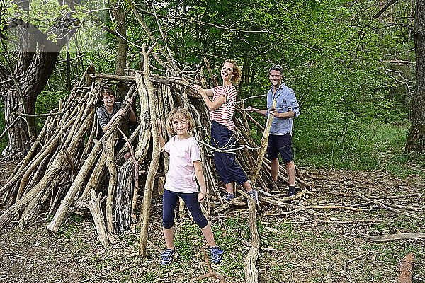 Familie lächelt beim Bau eines Lagers mit Baumstämmen im Wald