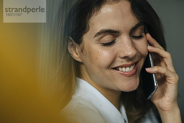 Junge Frau lächelt  während sie im Büro mit einem Mobiltelefon spricht
