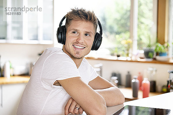 Lächelnder Geschäftsmann  der über Kopfhörer Musik hört  während er am Schreibtisch im Büro sitzt