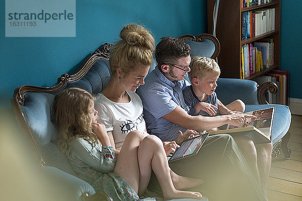 Familie schaut sich ein Fotoalbum an  während sie auf dem Sofa im Wohnzimmer sitzt