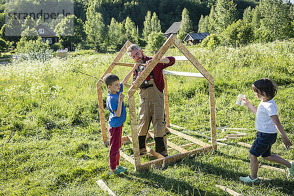 Kinder helfen einem Zimmermann beim Bau eines Spielhauses an einem sonnigen Tag