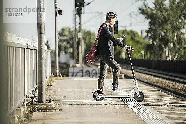 Mann  der sein Smartphone benutzt  während er mit seinem Roller am Bahnsteig wartet