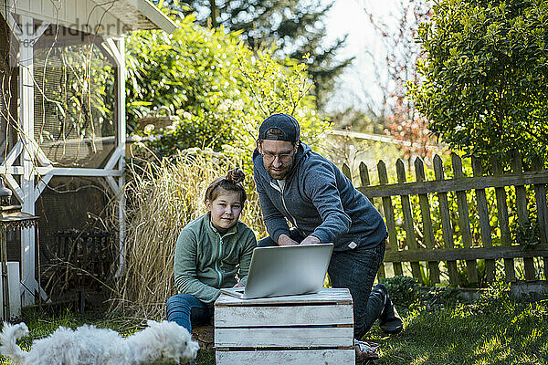 Vater unterrichtet Tochter  während er im Hof einen Laptop benutzt
