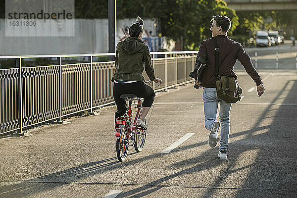 Junger Mann  der ein Skateboard trägt  während er an seiner Freundin vorbeirennt  die in der Stadt Fahrrad fährt