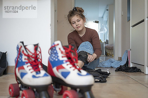Mädchen betrachtet Rollschuh  während sie zu Hause auf dem Boden sitzt