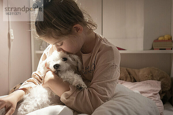 Nettes Mädchen umarmt Hund  während im Schlafzimmer sitzen