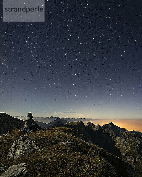 Deutschland  Bayern  Mann sitzt auf dem Gipfel der Ammergauer Hochplatte in der Abenddämmerung