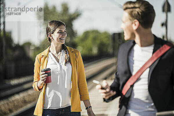 Lächelnde Frau mit wiederverwendbarem Kaffeebecher  die beim Gehen am Bahnsteig wegschaut