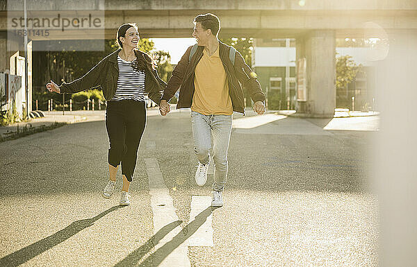 Unbekümmertes junges Paar  das sich beim Laufen auf der Straße in der Stadt an den Händen hält