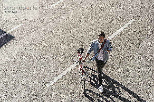 Junger Mann überquert Straße mit Fahrrad in der Stadt