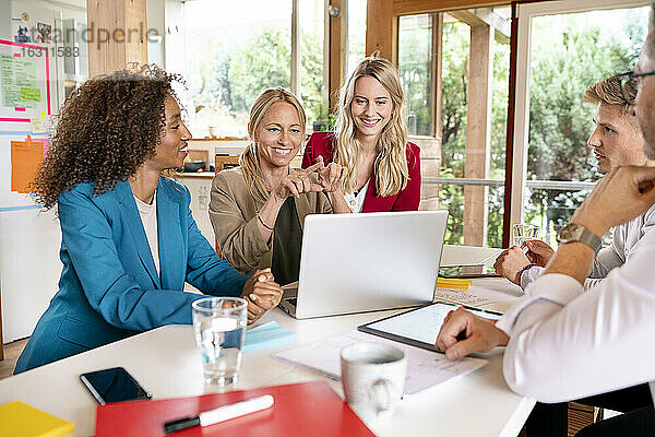 Männliche und weibliche Geschäftsleute  die in einer Besprechung über einen Laptop auf dem Schreibtisch diskutieren