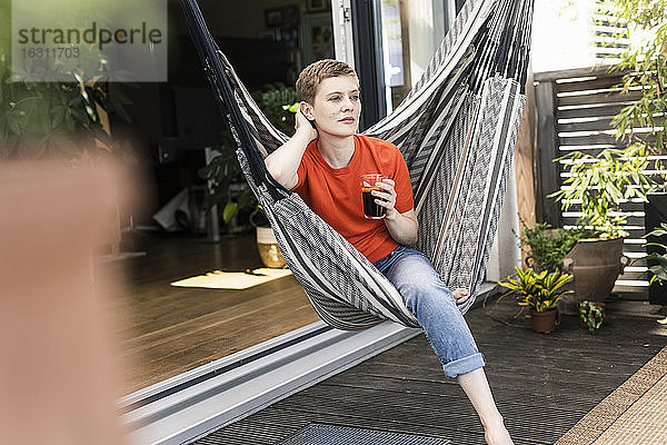 Nachdenkliche erwachsene Frau mit Kaffee in der Hand auf einer Schaukel auf der Veranda sitzend