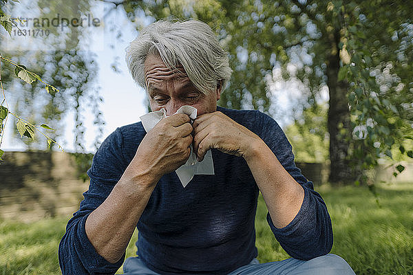 Runzliger Mann schnäuzt sich die Nase  während er auf einem Feld sitzt