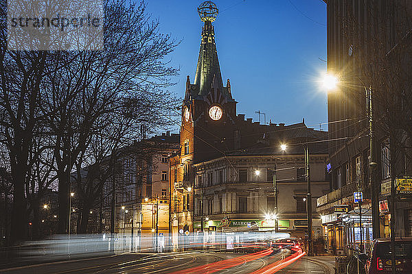 Polen  Kleinpolen  Krakau  Beleuchtete Stadtstraße mit Uhrturm bei Nacht