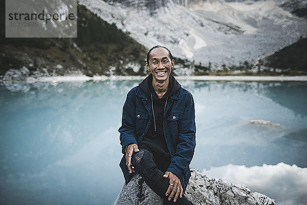 Italien  Südtirol  Cortina d Ampezzo  Sorapis-See  Porträt eines jungen Mannes  der auf einem Felsen am Bergsee sitzt