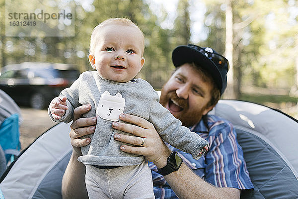 Lächelnder Mann hält kleinen Sohn (6-11 Monate) auf Camping  Wasatch-Cache National Forest
