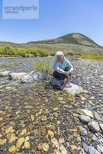 USA  Idaho  Sun Valley  Frau sitzt auf einem Felsen im Fluss