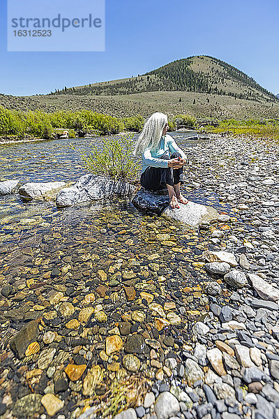 USA  Idaho  Sun Valley  Frau sitzt auf einem Felsen im Fluss