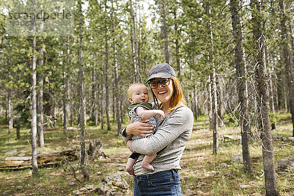 Porträt einer lächelnden Frau  die ihren kleinen Sohn (6-11 Monate) im Wald hält  Wasatch Cache National Forest