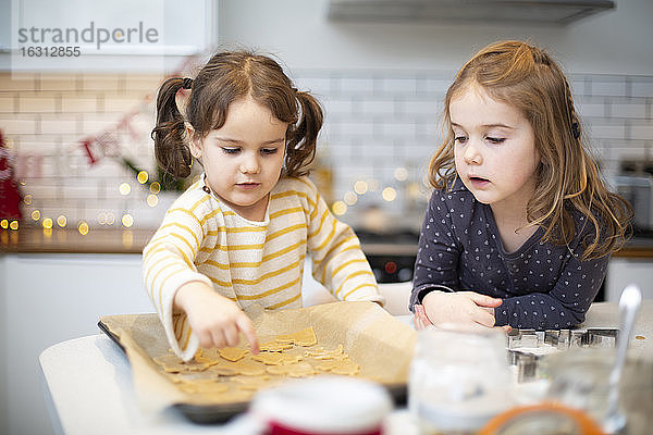 Zwei Mädchen stehen in der Küche und backen Weihnachtsplätzchen.