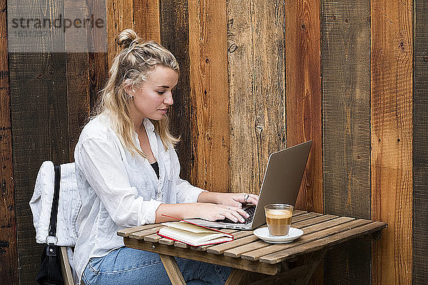 Junge blonde Frau mit Gesichtsmaske und Laptop-Computer  die aus der Ferne arbeitet.