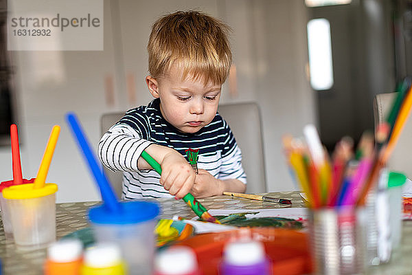 Dreijähriger Junge  der zu Hause mit Töpfen und Pinseln malt.