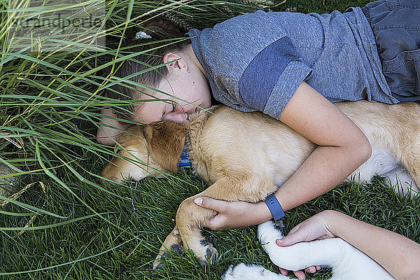 Zwei Mädchen im Teenager-Alter liegen auf dem Rasen und umarmen ihre Golden Retriever-Hunde.