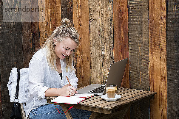 Junge blonde Frau sitzt allein an einem Café-Tisch mit einem Laptop-Computer