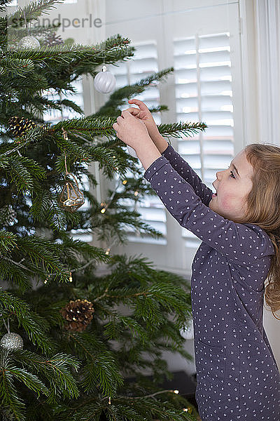 Junges Mädchen schmückt Weihnachtsbaum mit Christbaumkugeln.