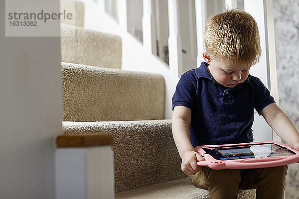 Ein dreijähriger Junge saß auf der Treppe und betrachtete ein digitales Tablett.