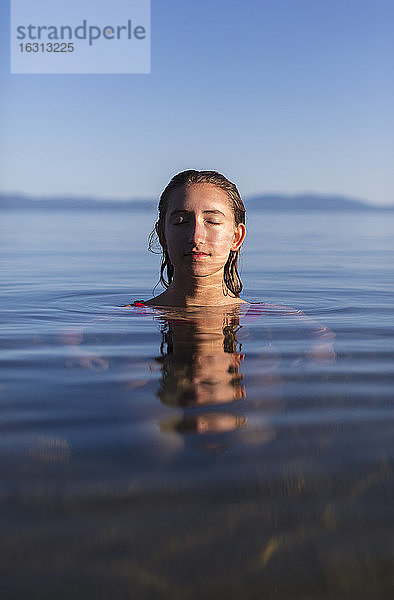 Teenager-Mädchen mit geschlossenen Augen  Kopf und Schultern in der Morgendämmerung über dem ruhigen Wasser eines Sees