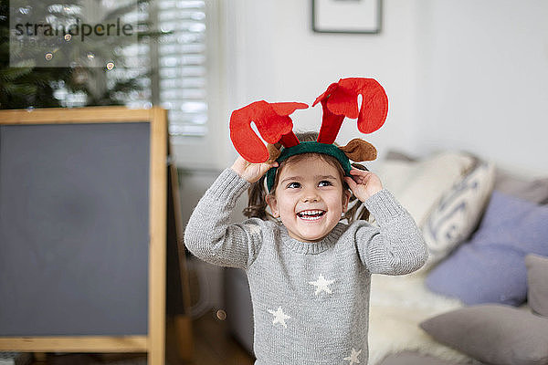 Lächelndes junges Mädchen mit grauem Pullover  das ein Rentiergeweih-Stirnband trägt.