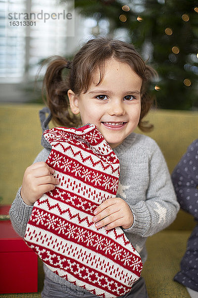 Junges Mädchen hält einen rot-weißen Weihnachtsstrumpf in der Hand und lächelt in die Kamera.