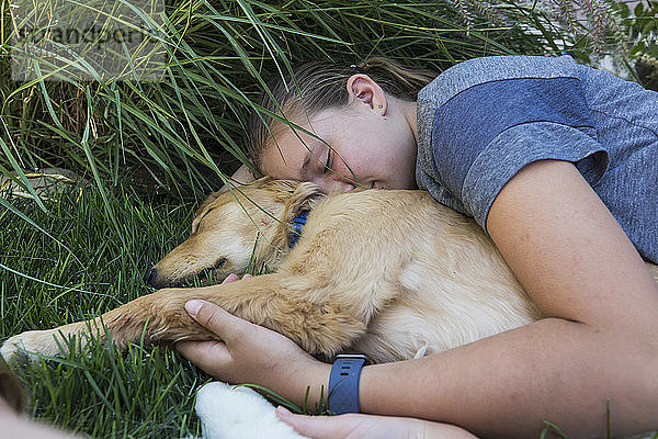 Teenagermädchen liegt auf dem Rasen und umarmt ihre Golden Retriever-Hunde.