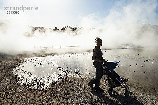 Eine Frau und ein Kind in einem Kinderwagen im aufsteigenden Dampf aus Thermalbecken