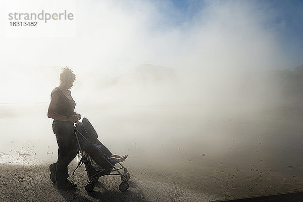 Eine Frau und ein Kind in einem Kinderwagen im aufsteigenden Dampf aus Thermalbecken