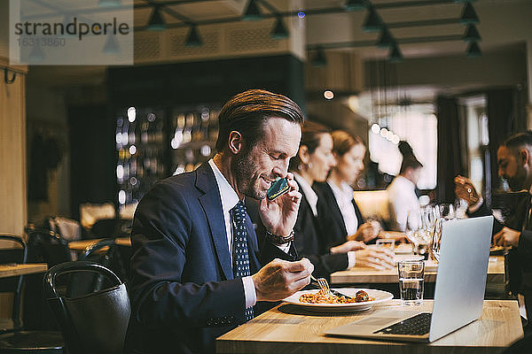 Lächelnder männlicher Geschäftsmann telefoniert beim Essen im Restaurant