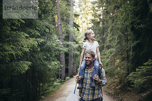 Lächelnder Vater trägt Tochter auf der Schulter beim Waldspaziergang