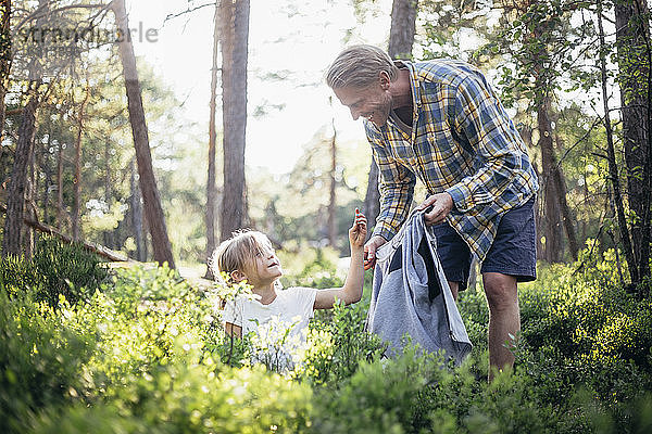Lächelnder Vater sieht Tochter beim Müllsammeln im Wald an