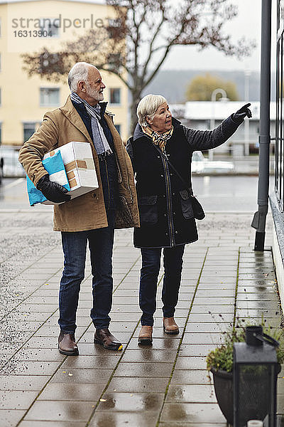 Ältere Frau  die im Winter von ihrem männlichen Partner mit einem Paket auf den Bürgersteig zeigt