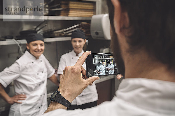 Männlicher Koch fotografiert weibliche Mitarbeiter in Großküche