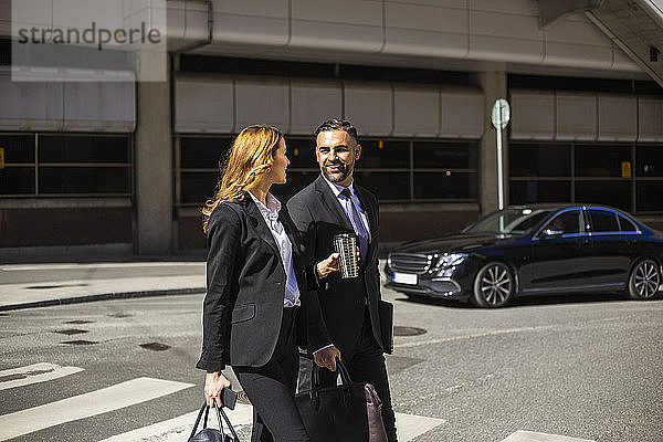 Lächelnde Geschäftsfrau und Geschäftsmann überqueren Straße in der Stadt