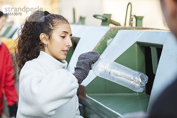 Lächelnde Umweltschützerin mit Freundin  die eine Plastikflasche in den Mülleimer wirft