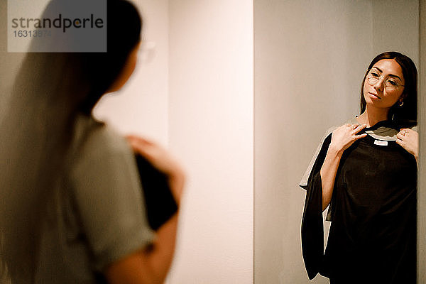 Junge Frau mit Kleidung schaut in den Spiegel im Modegeschäft